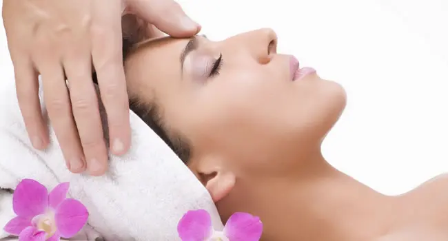 Relaxed woman receiving a head massage next to orchid flowers