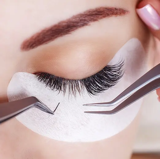 Lash technician applying volume eyelash extensions with tweezers and under-eye pads
