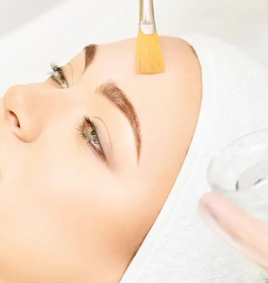 Aplicación de peeling con pincel en la frente de una clienta
