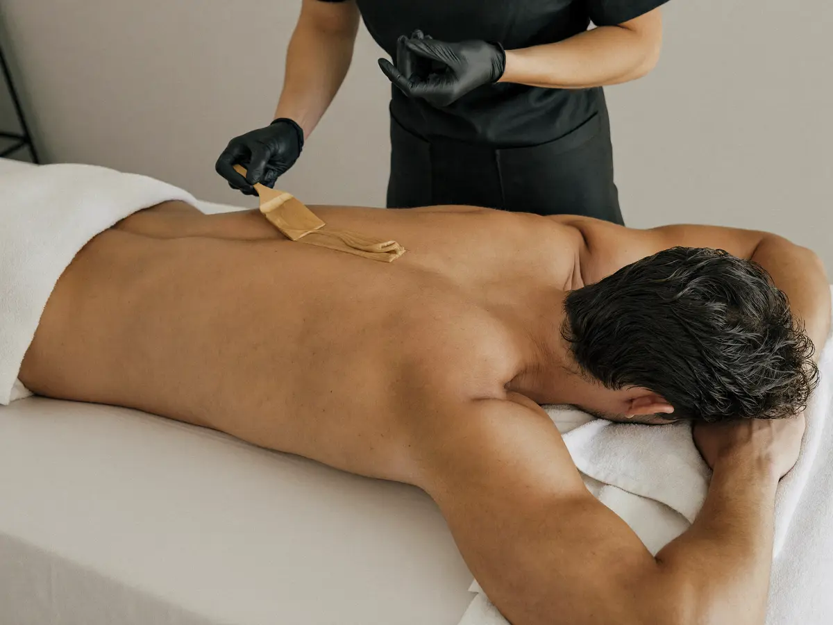 Esteticista aplicando cera tibia con espátula en la espalda de un hombre